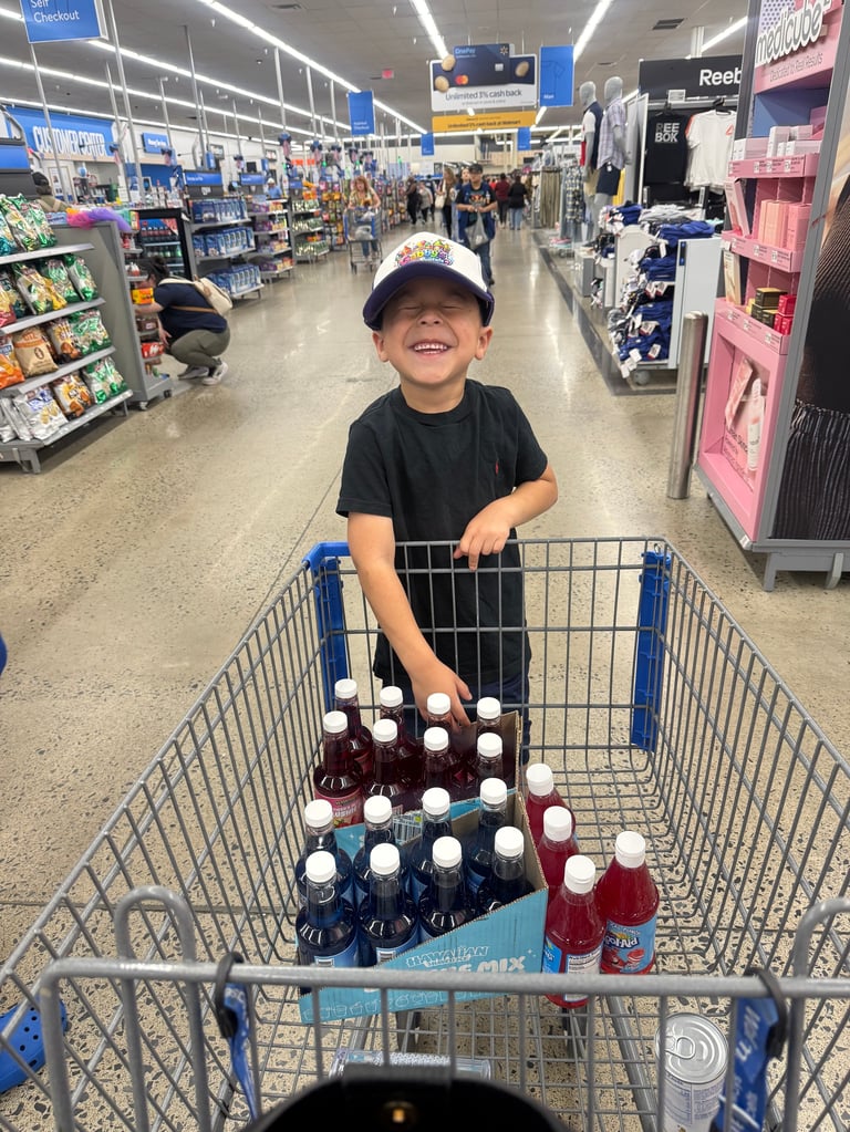 Young child in white and blue cap pushing shopping cart filled with beverages in a Walmart store aisle