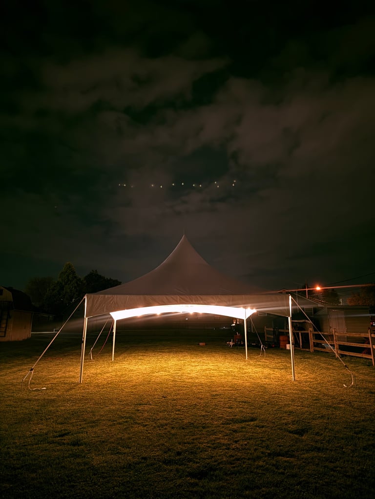 Illuminated tent structure at night on sandy ground with dark sky and trees in background