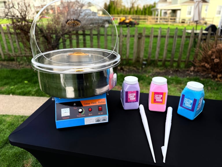 Cotton candy machine with three colored sugar bottles and two white sticks on a table in a backyard setting