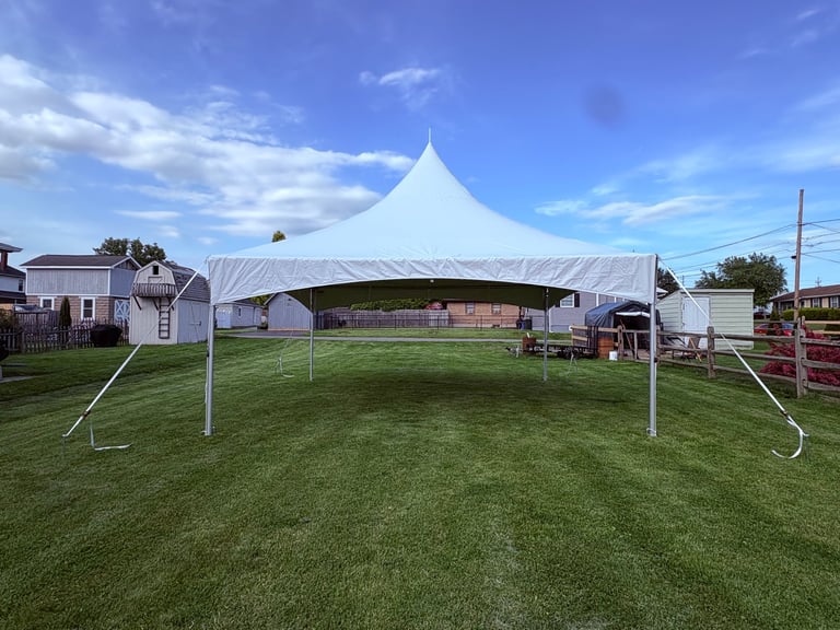 Large white tent with peaked roof set up in a green grass field under blue sky with support poles visible